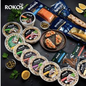 Компания Rokos Fish основана в 2019 году. Производственные мощности расположены в Республике Казахстан, 030000, город Актобе, район Астана, квартал Промзона, здание 2А. Компания специализируется на переработке морской рыбы с фокусом на производство готовых рыбных пресервов из сельди под собственными торговыми марками.
Производственные мощности и стандарты качества Rokos располагает современным производственно перерабатывающим комплексом, включающим:
•	зоны приёма и хранения сырья; 
•	участки первичной обработки (потрошение, разморозка/охлаждение); 
•	разделку, порционирование, соление и маринование; 
•	участки охлаждения, шоковой и IQF заморозки; 
•	автоматические линии фасовки и упаковки (включая термоформовочные линии MULTIVAC).
Стандарты и сертификация:
•	ISO 22000 (системы менеджмента безопасности пищевой продукции); 
•	Сертификат «Халяль».
Система качества включает лабораторный контроль, документооборот по прослеживаемости партии (traceability) и внутренние регламенты по входному контролю сырья.
Ассортимент рыбной продукции Rokos Fish выпускает широкий ассортимент пресервов и готовых продуктов из сельди, ориентированных на розничный рынок, HoReCa и опт. Основные бренды и позиции:
Торговая марка ROKOS FISH
•	Селедочка застольная в масле — 180 г, 500 г 
•	Селедочка «к картошечке» в масле — 180 г, 500 г 
•	Селедочка классическая в масле — 180 г, 500 г 
•	Селедочка с перцем в масле — 180 г, 500 г 
•	Селедочка с укропом в масле — 180 г, 500 г 
•	Селедочка Матье в масле — 150 г, 350 г 
•	Селедочка Оригинальная в масле — 150 г, 350 г 
•	Селедочка Норвежская в масле — 150 г, 350 г 
•	Филе сельди в масле — 500 г, 850 г 
•	Селедочка «Для сельди под шубой» — 500 г 
•	Филе сельди в термоформовочных лотках (MULTIVAC): 260 г, 400 г 
•	Филе/кусочки для салата «Под шуба»: 260 г, 400 г
Торговая марка «ТО ЧТО НАДО»
•	Селедочка застольная в масле — 150 г, 400 г 
•	Селедочка классическая в масле — 150 г, 400 г 
•	Селедочка Норвежская в масле — 150 г, 400 г 
•	Селедочка «По домашнему» в заливке — 150 г, 400 г
Дополнительные SKU и позиции
•	Селедочка в масле/пикантная/слабосолёная в разных фасовках (150–500 г); 
•	Продукция в различной упаковке — банки, вакуум, термоформованные лотки; 
•	Возможность производства под private label и адаптации рецептур под требования партнёра.
Объёмы производства и мощности
•	Производственная мощность: до 600 000 банок в месяц (приблизительно 7 млн банок в год). 
•	Средний объём переработки (план на 2025): около 4000 тонн. 
•	Ежедневный приём сырья: порядка 40 тонн. 
•	Производство адаптировано под партии различного объёма; возможна гибкая настройки рецептур и упаковок под заказчика.
Источники сырья и логистика
•	Сырьё: преимущественно импортная свежемороженая сельдь от проверенных поставщиков. 
•	Критерии отбора поставщиков: требуемая сертификация, стабильность поставок, качество сырья. 
•	Логистика: собственный или партнёрский холодильный транспорт с постоянным контролем температурного режима; складские холодильные камеры достаточной ёмкости для поддержания непрерывного цикла производства. 
•	Приём сырья сопровождается ветеринарно санитарными документами и протоколами контроля качества.
Упаковка, маркировка и private label
•	Типы упаковки: пластиковые контейнеры с крышкой, вакуумные пакеты, термоформованные лотки MULTIVAC. 
•	Маркировка соответствует требованиям: штрихкоды, сроки годности, условия хранения и инструкции по разморозке/использованию. 
•	Возможность фасовки и брендинга под private label для сетей и дистрибьюторов — подготовка макетов, тестовых партий и согласование рецептур.
Каналы сбыта и потенциальные партнёры
•	Основные каналы: розничные сети, оптовые покупатели, сегмент HoReCa (рестораны, кейтеринг), дистрибьюторы и экспортные партнёры. 
•	Rokos готова к сотрудничеству с Российскими сетями и оптовыми покупателями на основе долгосрочных контрактов, предоставляя стабильные объёмы и гибкие коммерческие условия.
Коммерческие условия сотрудничества (ориентировочные/по запросу)
•	Минимальные партии заказа: по согласованию (возможна отработка MOQ для сети и индивидуальные условия для контрактных партнёров). 
•	Условия поставки: возможно оформление EXW/FOB/CIF по согласованию с партнёром. 
•	Сроки выполнения заказов на индивидуальные партии: типично 3–21 день в зависимости от объёма и наличия сырья. 
•	Условия оплаты: обсуждаются в коммерческих предложениях; возможны отсрочки для постоянных партнёров.
Контроль качества и гарантия безопасности
•	Внедрены регламенты входного контроля сырья, технологического контроля на этапах переработки и финального контроля готовой продукции. 
•	Лабораторные исследования по микробиологическим и химическим показателям. 
•	Порядок рекламаций и возвратов: оформляется протоколом экспертизы партии и рассматривается в рамках действующего регламента компании.
Устойчивость и сертификаты
•	Наличие сертификата «Халяль» подтверждает соответствие религиозным требованиям при производстве и обработке продукции. 
•	ISO 22000 подтверждает стандарты управления безопасностью пищевой продукции. 
•	Rokos Fish работает с поставщиками с контролем качества поставляемой рыбы и стремится к стабильности поставок.
Преимущества для партнёров
•	Широкая линейка фасовок и рецептур под разные сегменты рынка. 
•	Высокая производственная мощность и стабильность объёмов. 
•	Соблюдение международных стандартов безопасности пищевой продукции. 
•	Гибкость в частотах партий и возможностях private label. 
•	Опыт работы с розницей и HoReCa, возможность адаптировать продукты под требования клиента.
Рекомендации для быстрого старта сотрудничества
•	Запросить коммерческое предложение и прейскурант по интересующим SKU. 
•	Заказать образцы продукции и тестовые партии для оценки качества и потребительских характеристик. 
•	Предоставить требования к упаковке/бренду, минимальные объёмы и желаемые сроки поставки для подготовки расчёта MOQ и условий.
Rokos Fish — надёжный производитель и поставщик рыболовных пресервов: от приёма импортной сельди до готовой продукции в нескольких фасовках и упаковках. Компания сочетает современные производственные линии, систему контроля качества и гибкий подход к партнёрам, что позволяет удовлетворять потребности розничных сетей, опта и HoReCa. Для оформления сотрудничества и запроса коммерческого предложения просьба направить список интересующих позиций, требуемые объёмы и контакт для отправки прайс листа и образцов.